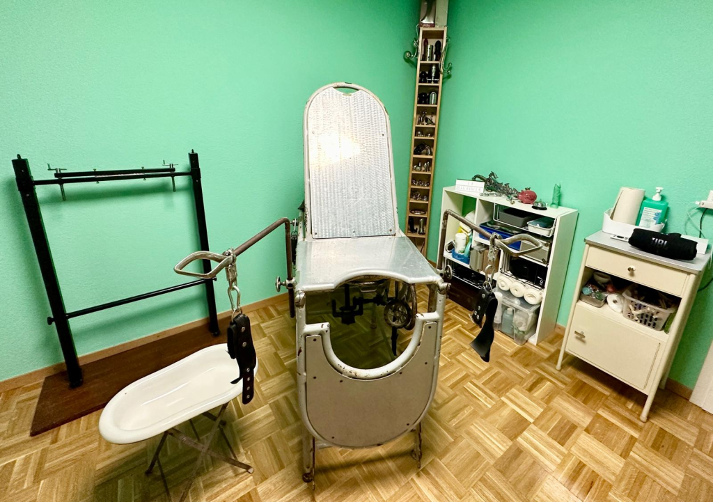 Vue d'ensemble de la salle médicale du donjon privé à Lausanne : table d'examen ancienne et rangements du matériel